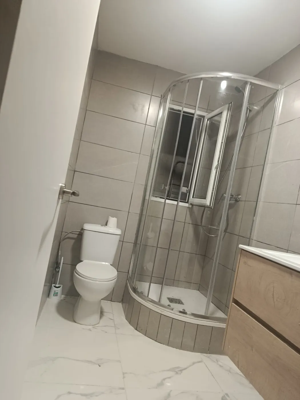 Baño con ducha angular de cristal y suelo de mármol claro