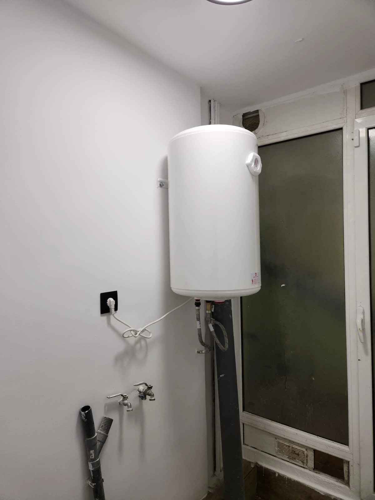 Trabajo de fontanería con instalación de termo eléctrico vertical blanco en una galería de Barcelona