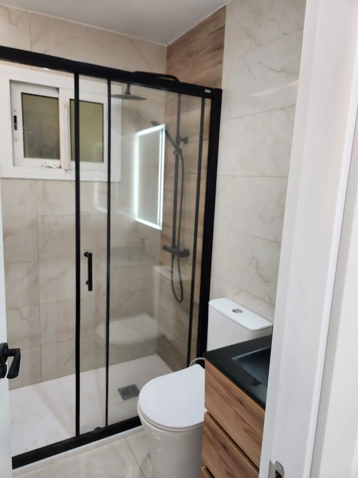 Reforma baño con mampara de perfilería negra y revestimiento cerámico efecto madera en Barcelona