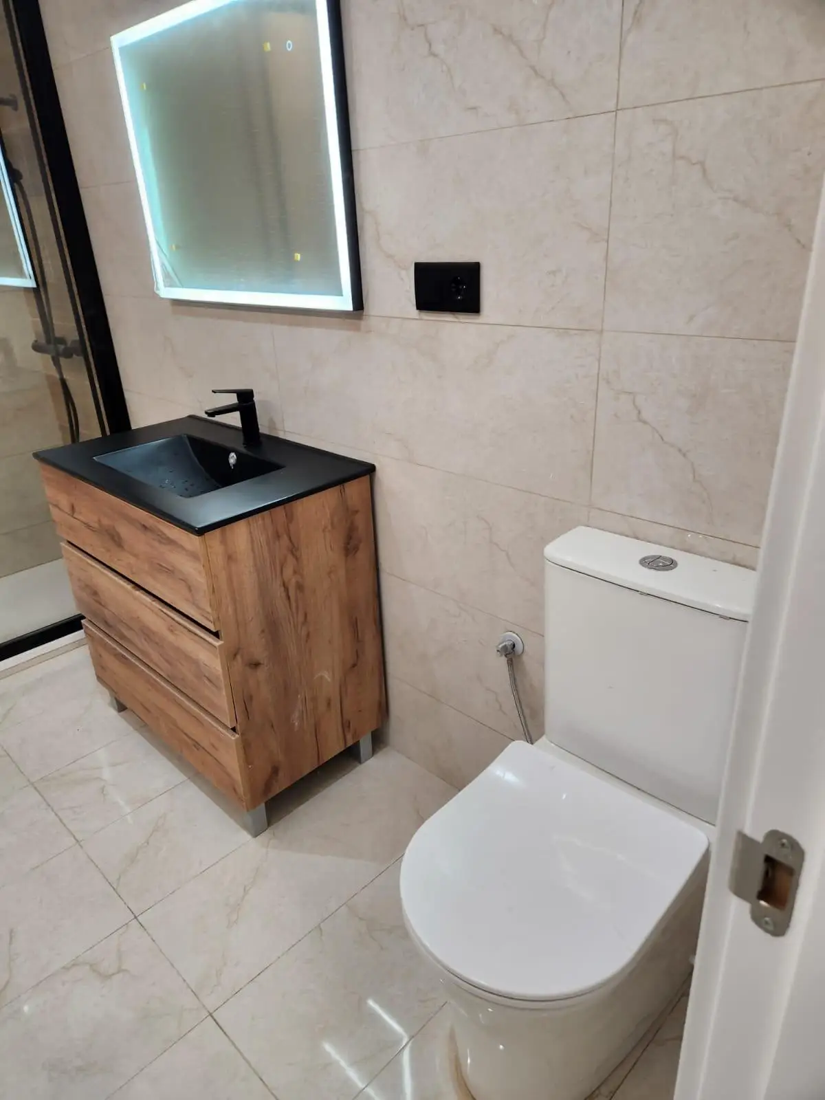 Reforma de baño con mueble de madera, lavabo negro y espejo retroiluminado en Barcelona