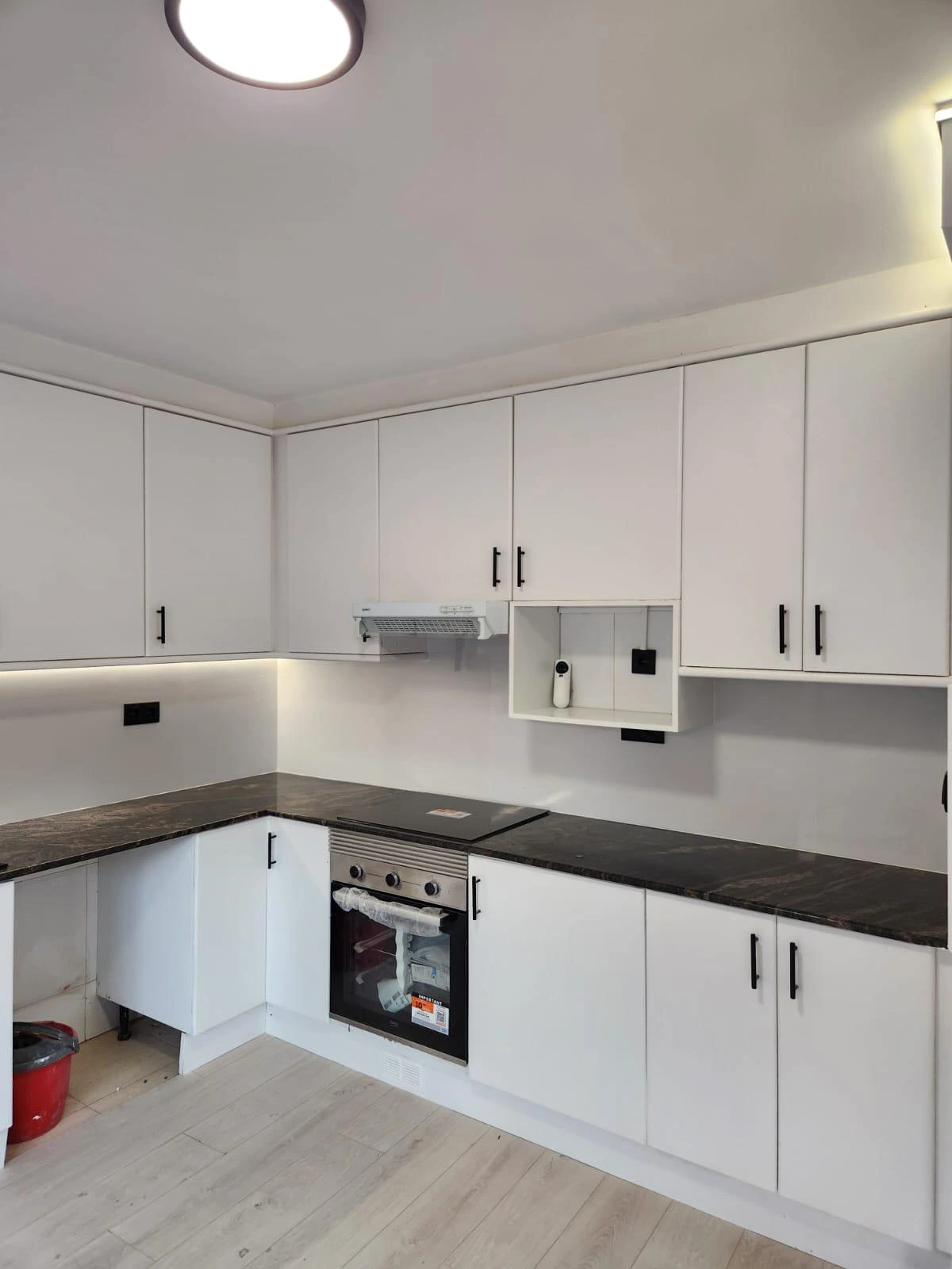 Reforma cocina con mobiliario blanco minimalista y encimera de granito oscuro en Barcelona
