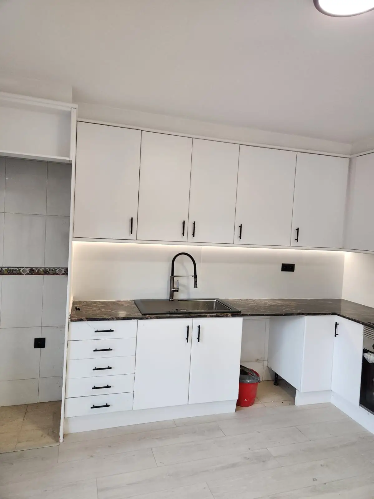 Reforma de cocina con mobiliario blanco mate, tiradores negros y encimera de piedra oscura en Barcelona